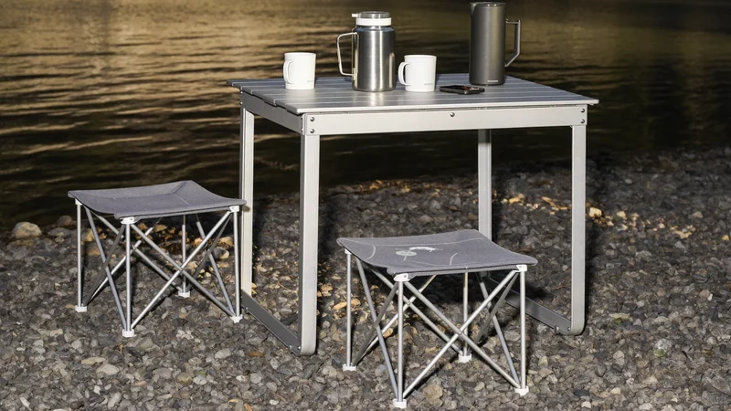 Klapptisch und zwei Hocker am Seeufer bei goldenem Licht mit Thermoskanne